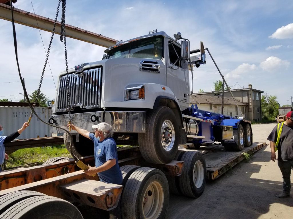 photo of loading a roll off truck onto a flatbed trailer using overhead bridge cranes