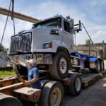 photo of loading a roll off truck onto a flatbed trailer using overhead bridge cranes